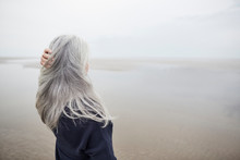 Senior Woman With Hand In Long Gray Hair On Winter Beach
