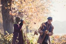 Playful Senior Couple Throwing Autumn Leaves In Sunny Park