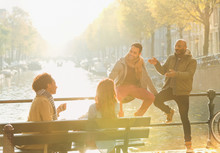 Young Friends Talking, Hanging Out On Sunny Urban Autumn Bridge Over Canal, Amsterdam