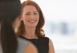 © Martin Barraud/Caia Image - Smiling businesswoman with red hair talking to colleague