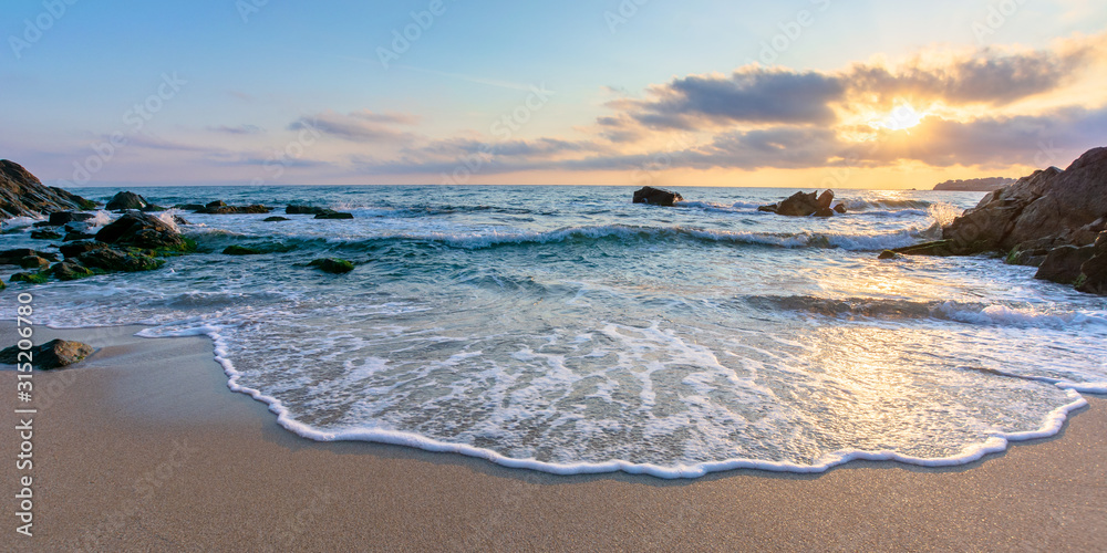 sunrise on the beach. beautiful summer scenery. rocks on the sand. calm waves on the water. clouds on the sky. wide panoramic view - obrazy, fototapety, plakaty 
