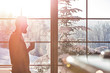 © Rafal Rodzoch/Caia Image - Man drinking coffee at sunny window with view of snowy trees