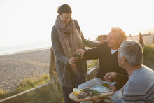 Mature Friends Drinking Wine And Enjoying Barbecue On Sunset Beach