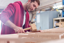Male carpenter using wood mallet on boat in workshop