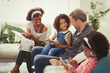 © Paul Bradbury/Caia Image - Multi-ethnic young family using digital tablets reading magazine on sofa