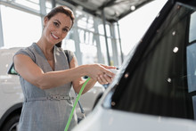 Portrait Smiling, Confident Female Customer Charging Hybrid Car In Car Dealership Showroom
