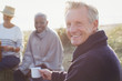 © Sam Edwards/Caia Image - Portrait smiling senior man drinking coffee friends on sunny beach