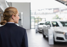 Blonde Car Saleswoman Looking Away In Car Dealership Showroom