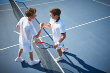Young Male Tennis Players Handshaking At Tennis Net On Sunny Blue Tennis Court