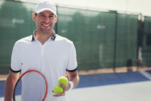 Portrait Confident, Smiling Young Male Tennis Player Holding Tennis Racket Tennis Balls On Sunny Tennis Court