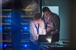 © Agnieszka Olek/Caia Image - IT technicians working at laptop in dark server room