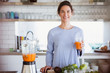 © Sam Edwards/Caia Image - Portrait confident, smiling woman drinking healthy carrot juice in kitchen