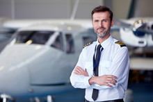 Portrait Confident Male Pilot Standing Near Airplane In Hangar