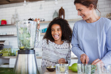 Mother and daughter making healthy green smoothie in blender in kitchen