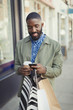 © Caiaimage/Paul Bradbury/Caia Image - Smiling young man coffee shopping bags texting cell phone on urban sidewalk