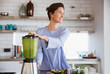 © Sam Edwards/Caia Image - Smiling brunette woman making healthy green smoothie in blender in kitchen