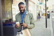 © Caiaimage/Paul Bradbury/Caia Image - Young man coffee shopping bags texting cell phone on urban sidewalk