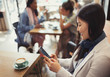 © Caiaimage/Paul Bradbury/Caia Image - Smiling young woman texting cell phone drinking coffee at cafe table