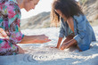 © Sam Edwards/Caia Image - Mother and daughter drawing spirals in sand on summer beach