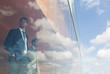 © Caiaimage/Martin Barraud/Caia Image - Pensive businessmen looking out modern office window at sunny blue sky clouds