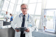 © Agnieszka Olek/Caia Image - Portrait confident senior male doctor with clipboard in hospital lobby