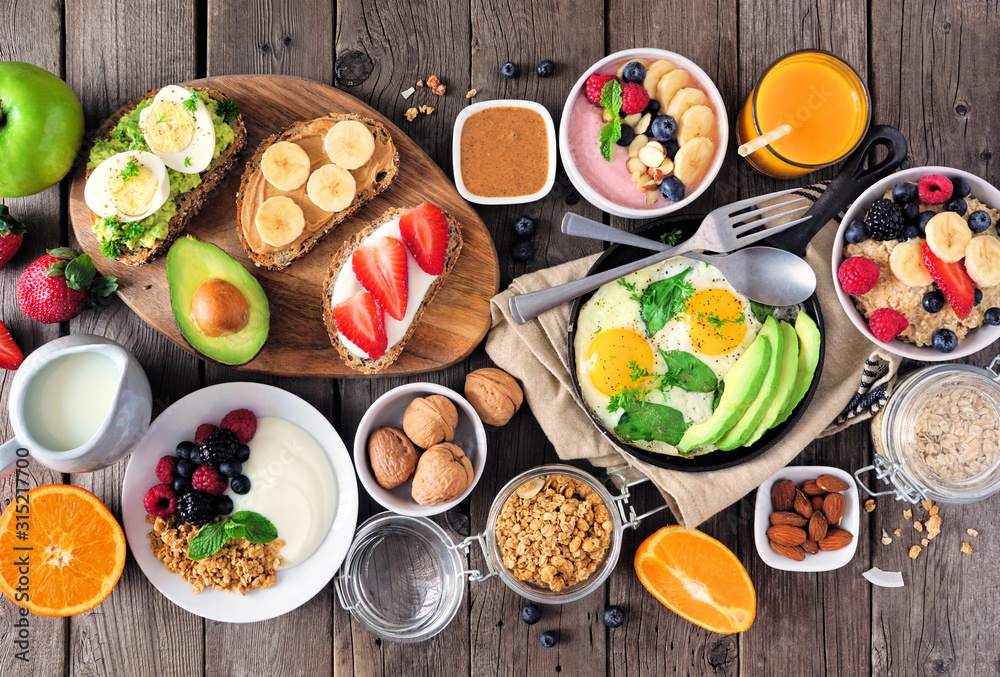 Healthy breakfast table scene with fruit, yogurts, oatmeal, smoothie, nutritious toasts and egg skillet. Top view over a wood background. - obrazy, fototapety, plakaty 
