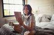 © Caiaimage/Paul Bradbury/Caia Image - Smiling young woman headphones drinking coffee using digital tablet on bed