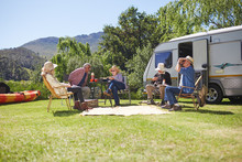 Active Senior Friends Relaxing Outside Camper Van At Sunny Summer Campsite