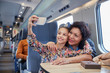 © Agnieszka Olek/Caia Image - Affectionate mother daughter taking selfie camera phone on passenger train