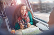 © Agnieszka Olek/Caia Image - Smiling young woman with camera and map riding passenger train