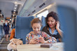 © Agnieszka Olek/Caia Image - Mother daughter sharing headphones, listening to music smart phone on passenger train