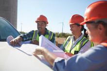Engineers Reviewing Blueprints On Truck At Sunny Wind Turbine Power Plant