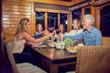 © Trevor Adeline/Caia Image - Friends toasting red wine glasses, enjoying dinner at cabin dining room table