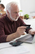 © Robert Daly/Caia Image - Focused senior man with credit card paying bills at laptop