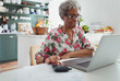 © Robert Daly/Caia Image - Senior woman paying bills at laptop in kitchen