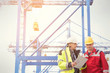 © Rafal Rodzoch/Caia Image - Dock worker and manager with clipboard talking below crane at shipyard
