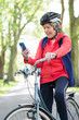 © Robert Daly/Caia Image - Active senior woman using smart phone on bike in park