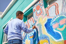 Male Volunteer Painting Vibrant Mural On Sunny Wall