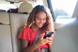 © Sam Edwards/Caia Image - Tween girl using smart phone in back seat of car
