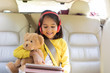 © Sam Edwards/Caia Image - Smiling girl teddy bear using digital tablet headphones in back seat of car