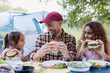 © Sam Edwards/Caia Image - Father and daughters enjoying barbecue hamburger lunch at campsite