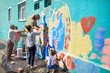 © Trevor Adeline/Caia Image - Community volunteers painting multicolor mural on sunny urban wall