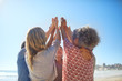 © Trevor Adeline/Caia Image - Women friends raising hands in circle during yoga retreat on sunny beach