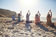 © Trevor Adeline/Caia Image - Group practicing yoga on sunny beach during yoga retreat
