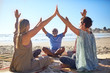 © Trevor Adeline/Caia Image - Group joining hands in circle on sunny beach during yoga retreat