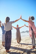 © Trevor Adeline/Caia Image - Group joining hands in circle on sunny beach during yoga retreat