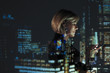 © Paul Bradbury/Caia Image - Double exposure businesswoman using smart phone against highrise lights at night