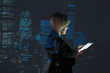 © Paul Bradbury/Caia Image - Double exposure businesswoman using digital tablet against highrise lights at night