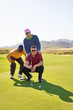 Male golfers planning putt shot on sunny golf course putting green