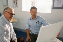 Male Doctor Meeting With Senior Patient At Computer In Doctors Office